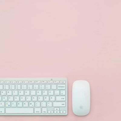 A clean and minimalist flat lay of a white keyboard and mouse on a pastel pink background. Perfect for feminine office themes.
