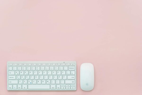 A clean and minimalist flat lay of a white keyboard and mouse on a pastel pink background. Perfect for feminine office themes.