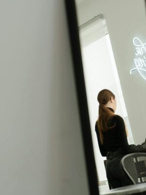 Woman working on a laptop in a sleek modern studio with a neon sign reflection.