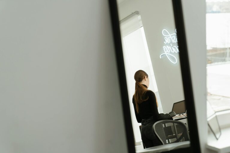 Woman working on a laptop in a sleek modern studio with a neon sign reflection.